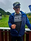 Eldre mann i blå jakke står ute ved et rekkverk med grønt landskap bak.