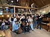 En gruppe mennesker poserer inne i en trelåve med instrumenter, lyslenker og publikum i bakgrunnen.
