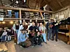En gruppe mennesker poserer inne i en trelåve med instrumenter, lyslenker og publikum i bakgrunnen.