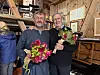 To menn står innendørs i en låve og holder hver sin blomsterbukett.