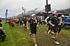 Løpere i svart sportsutstyr løper ut fra startområdet på et vått gressfelt.
