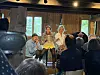 Tre personer opptrer foran publikum i en låve med trevegger og vinduer.