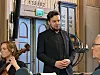En mann står foran publikum i en kirke mens en kvinnelig musiker sitter med et strykeinstrument.