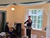 Fiolinist spiller ved notestativ i et rom med piano og store vinduer.