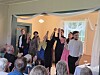 En gruppe mennesker står foran publikum i et pyntet rom og løfter hendene under en feiring.