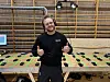 En mann smiler og gir tommelen opp foran en arbeidsbenk i en hall.