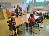 Barn sitter rundt et bord i et klasserom med en voksen som står ved siden av.