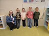 Fem barn står foran en tavle i et klasserom mens en voksen kneeler ved siden av.