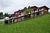 En gruppe mennesker står på en gressbakke foran en rød bygning med skog i bakgrunnen.