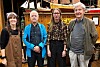 Fire personer står foran en historisk trebåt i et innendørs miljø.
