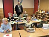 Barn sitter ved pulter i et klasserom, mens en mann med ordførerkjede står i bakgrunnen.