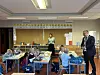 Lærer står ved siden av elever som sitter ved bord i et klasserom.