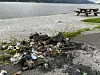 Bålrester og søppel på en grusstrand ved vannet.
