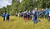 Mennesker samlet i et gresskledd område ved skogkanten med turutstyr og sekker.