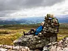 En person sitter og hviler ved en steinvarde med utsikt over fjell og daler.