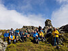 En gruppe turgåere står samlet på en fjellknaus med steinrøyser og blå himmel i bakgrunnen.