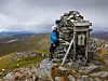Turgåer ved en steinvarde på en fjelltopp med stav og vid utsikt i bakgrunnen.