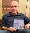 Mann sitter og holder en bok om apotekshistorie med illustrert bokomslag.