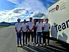 En gruppe personer står på en vei ved siden av en hvit buss med Teamster-logo.