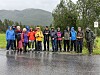 Gruppe turgåere i regntøy på en våt vei foran skogkledde fjell.
