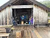 Mennesker samles i en gammel trehytte foran et grønt fjellandskap.