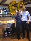 To personer står sammen ved en bar, omgitt av gullballonger med tallet 60.