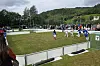 Barn spiller fotballkamp på en gressbane med skogkledde åser i bakgrunnen.
