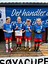 Fire unge fotballspillere i blå drakter står med medaljer og premier foran en bannervegg.