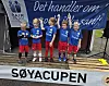Ungt fotballag med medaljer poserer foran en sponsorvegg ved Søya-cupen.