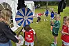 Barn i fotballdrakter samles rundt et fargerikt lykkehjul på en gressbane.