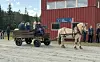 Lys hest trekker en vogn med passasjerer foran en rød bygning.