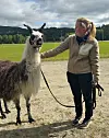 Lama og kvinne på en grussti ved et grønt jorde.