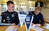 To menn signerer dokumenter ved siden av vimpler for Surnadal IL og Kristiansund Ballklubb.
