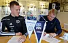 To menn signerer dokumenter ved siden av vimpler for Surnadal IL og Kristiansund Ballklubb.