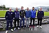 Seks menn i treningsklær står samlet ved en fotballbane.