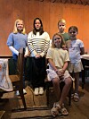 Fem barn poserer sammen i et rustikt rom med trevegger og stoler.