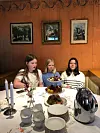 Tre personer ved et festdekket bord med mat, stearinlys og servise i en trepanelkledd spisestue.