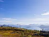 Fjellandskap med høstfarget lyng, blå fjellrygger og klar himmel.