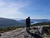 Turgåer med hund på et fjellplatå med utsikt over innsjø og fjell.