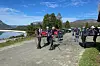 Turgåere samles på en grusvei ved et fjellvann i fjellandskap.