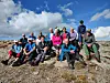 Turgruppe poserer på et steinete fjell under blå himmel og skyer.