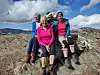 Fire turgåere poserer på et steinete fjellplatå under en blå himmel.