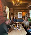 Flere voksne turgåere sitter rundt bord i ei stue med tømmervegger.