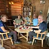 Fire menn sitter rundt et bord med mat og drikke i en tre­kledd stue.
