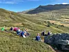 Gruppe fjellvandrere sitter i lyngen under en blå himmel med fjell i bakgrunnen.