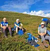 Fjellvandrere sitter i lyngen med ryggsekker i et åpent fjellandskap.