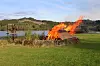Stort bål med flammer på en gresslette ved en innsjø.