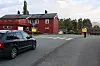 Mørk bil på vei forbi en rød bygning under en delvis skyet himmel.