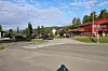 Veikryss med gangfelt, biler, bolighus og en rød trebygning under blå himmel.