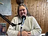 Kvinne med strikket genser sitter foran en mikrofon i et trepanelkledd rom.